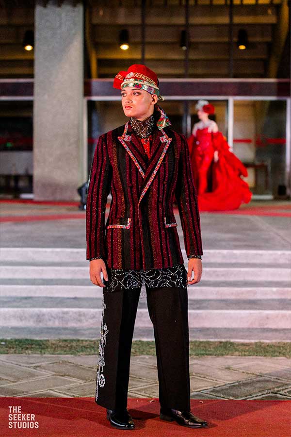 Model in a traditional embroidered suit with red accents by Amir Sali at a fashion show