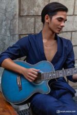 Man in a navy blue linen suit playing guitar, featuring a double-breasted jacket and loose-fitting trousers