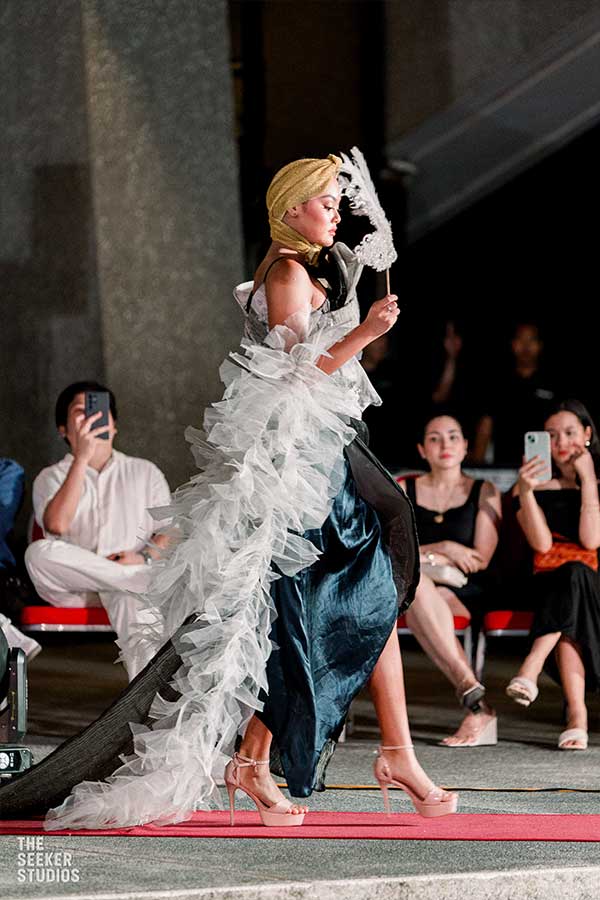 Model in a flowing gown with a ruffled white train and gold headscarf