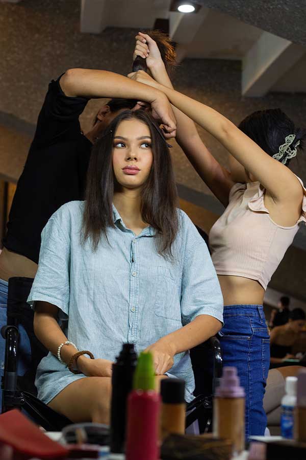 Model sits while stylists work on her hair during final preparations for a fashion show