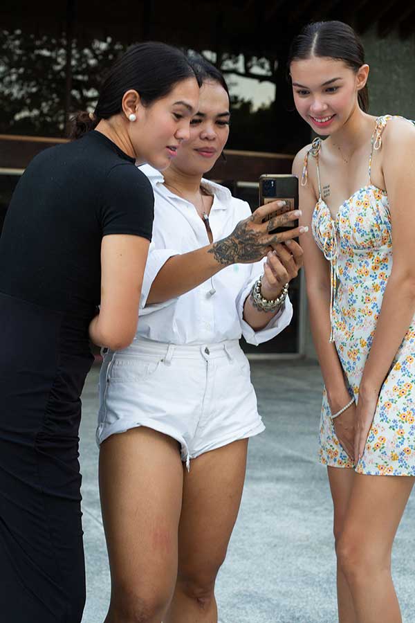 Josip Tumapa showing two models a picture on his phone during fashion show rehearsals
