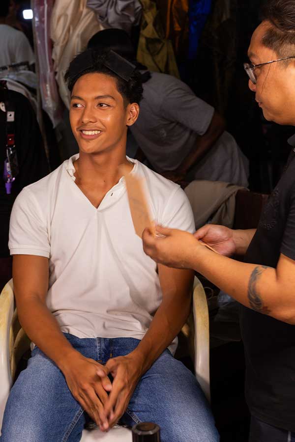 Male model smiling as makeup artist Ian Roy applies final touches backstage