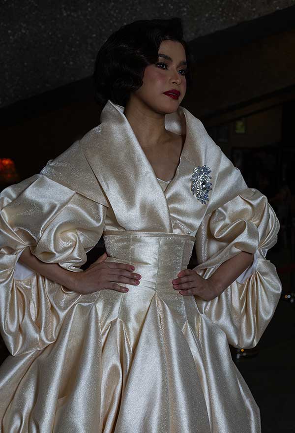 Model wearing a cream-colored dress with voluminous sleeves by Josip Tumapa backstage before