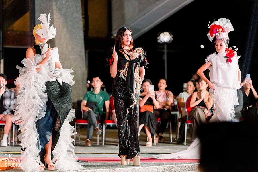 Three models in avant-garde outfits at a fashion show, featuring bold designs and flowing fabrics