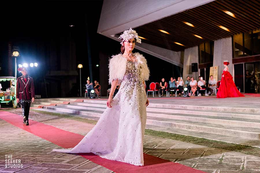 Model in an elegant white gown with feathered shoulders and floral headpiece walking the runway at Dumaguete fashion event