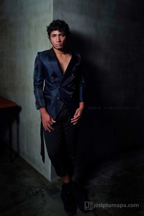 Full-body view of a menswear ensemble with a deep-cut jacket and straight trousers creating a long vertical line