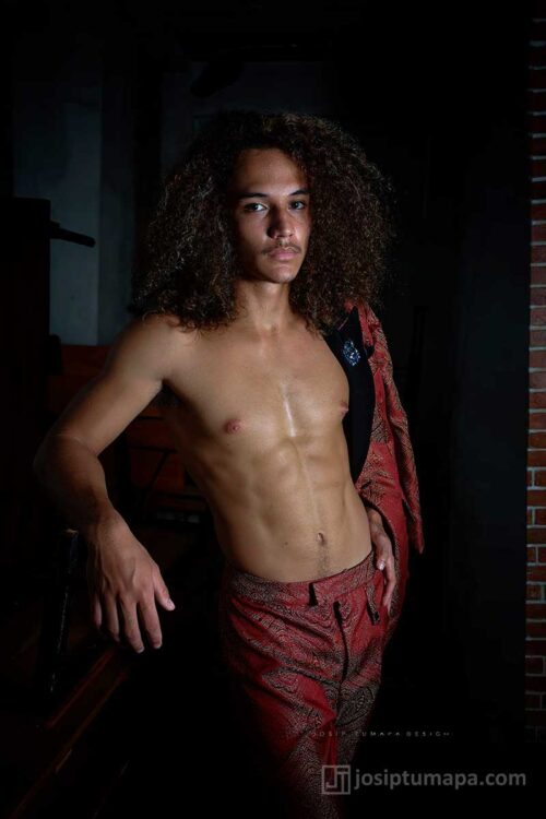 Bare torso with red trousers and jacket resting on the shoulder, paired with a relaxed stance and direct evening presence