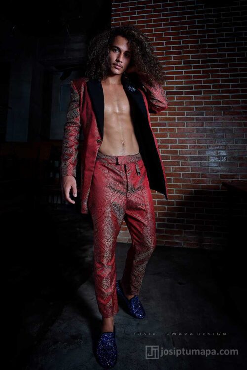 Unfastened red jacket worn on the body with bare torso and straight trousers, forming a dynamic modern evening menswear look