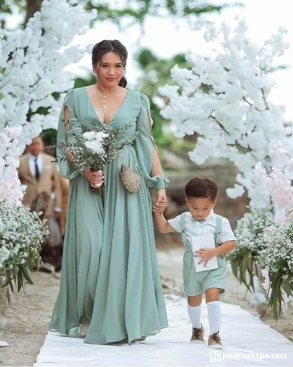 Mother in a custom-made mint green gown holding child’s hand at an outdoor event