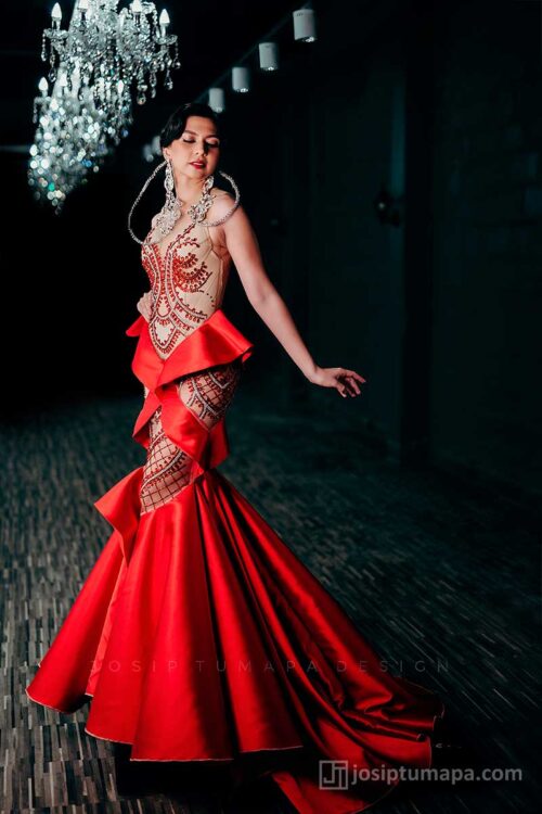 Side profile of red evening dress highlighting directional satin panels, elongated silhouette, and movement
