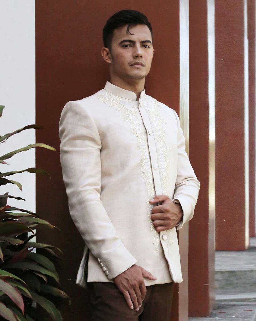Man in cream Coat Barong with embroidery, standing by modern architecture and plants, perfect for Filipino weddings