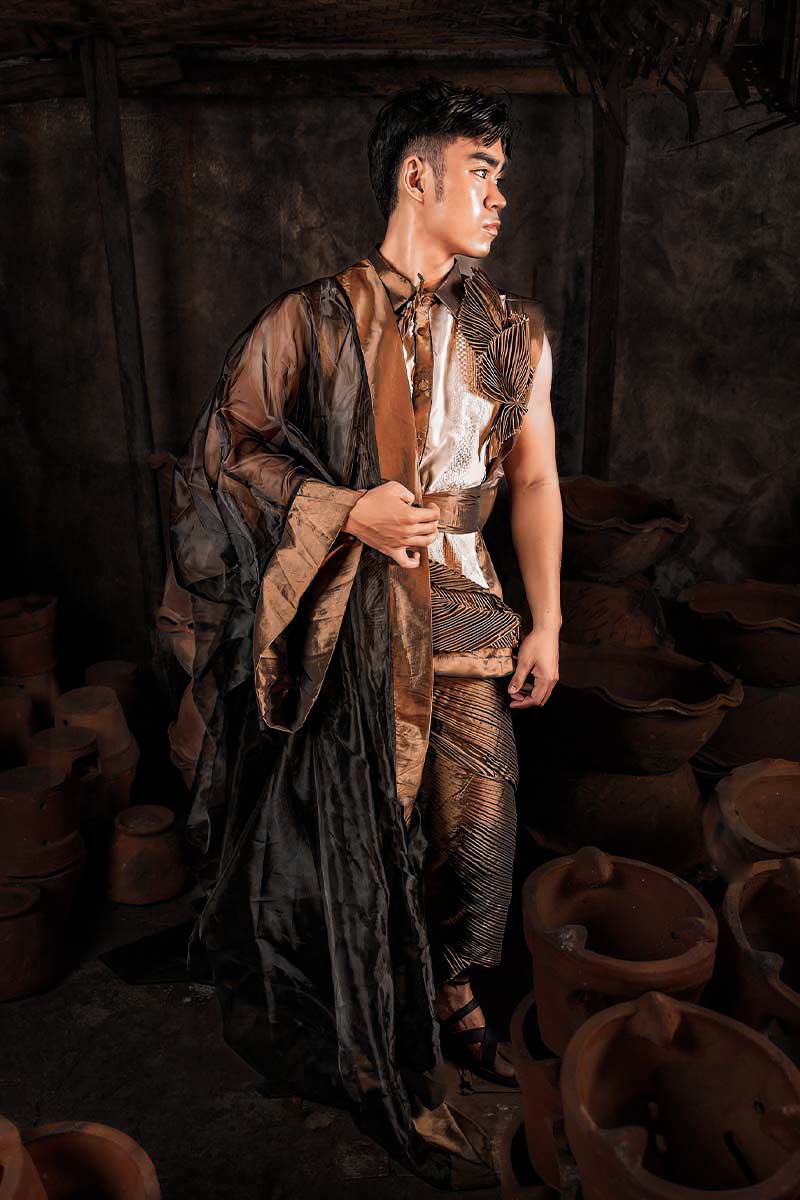 Male Filipiniana-inspired ensemble in bronze-gold tones with pleating and asymmetrical draping, photographed in a pottery workshop