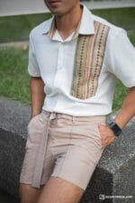 Model seated in soft beige shorts and white tribal shirt