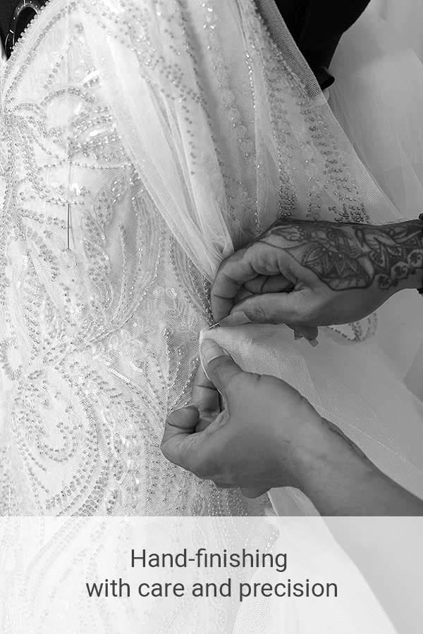 Close-up of tailor’s hands finishing details on a beaded bridal dress