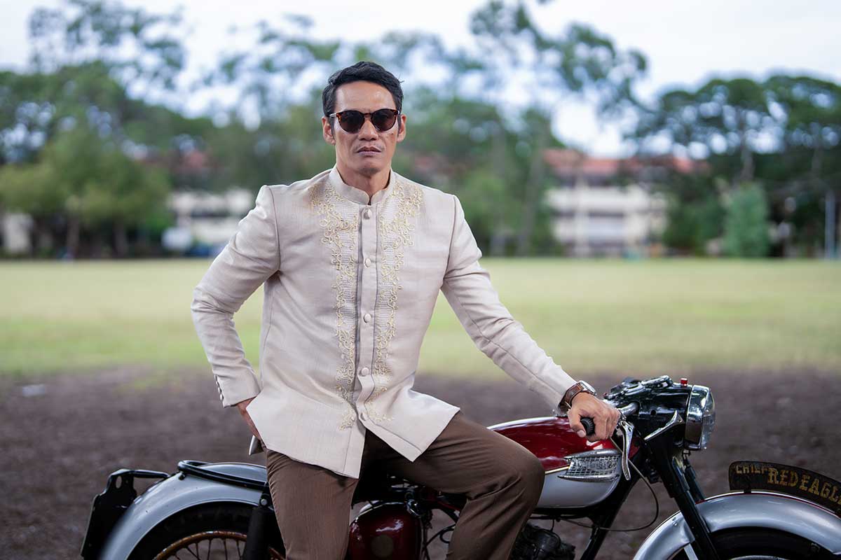 Man in embroidered Barong Tagalog beside vintage bike outdoors