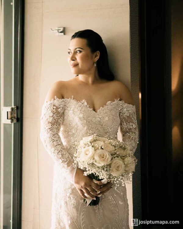 Bride in custom-made lace wedding dress holding bouquet of roses