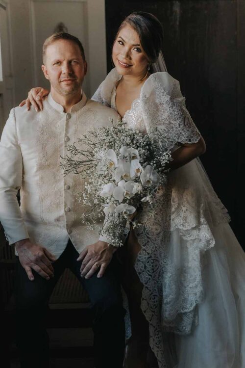 Bride in a custom Filipiniana Terno wedding gown with intricate lace beside groom in Barong Tagalog