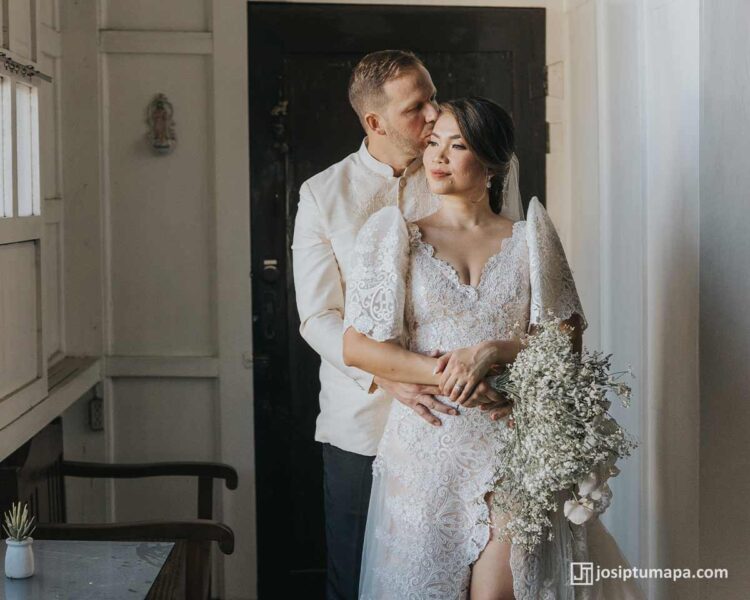 Groom embracing bride in Filipiniana lace wedding gown with butterfly sleeves during indoor wedding moment