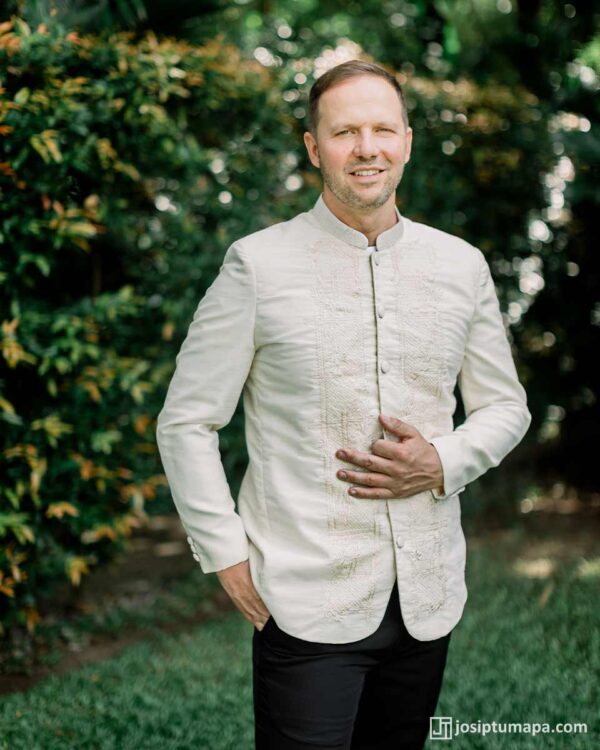 Groom in custom Piña Cocoon Silk Coat Barong Tagalog standing outdoors in tropical garden