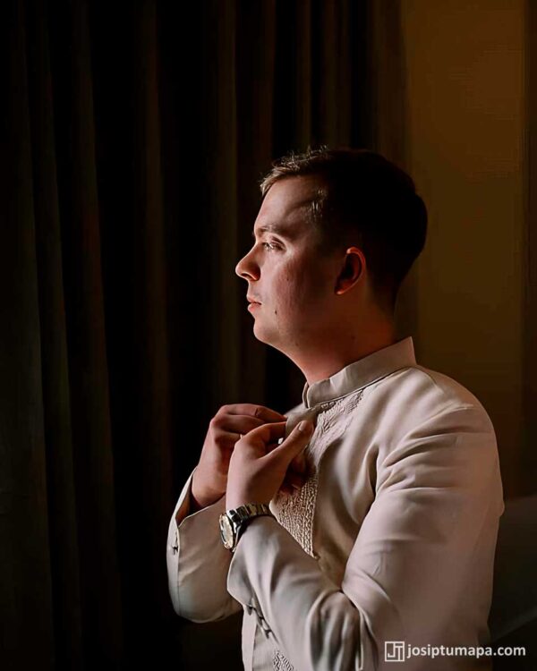 Groom buttoning his handcrafted Piña Silk Barong Tagalog in soft wedding light
