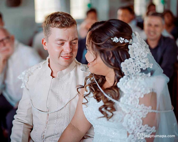 Bride and groom seated during wedding ceremony wearing Barong Tagalog and lace veil