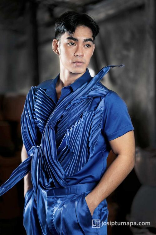 Men’s runway ensemble with satin draped panels, pleated construction, and structured surface detailing in deep azure
