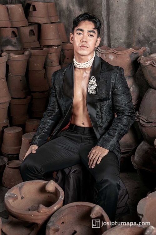 Open black jacquard silk jacket with pearl choker and brooch, seated
