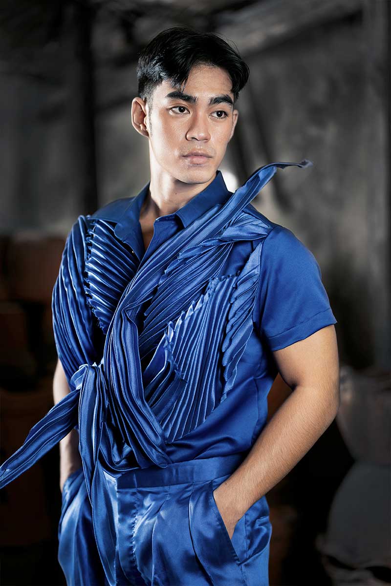 Men’s satin runway look with asymmetric draping, pleated surface accents, and layered construction in rich azure tones