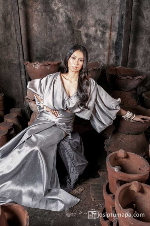 Satin gown in silver-gray with sculptural sleeves and draped skirt, seated pose