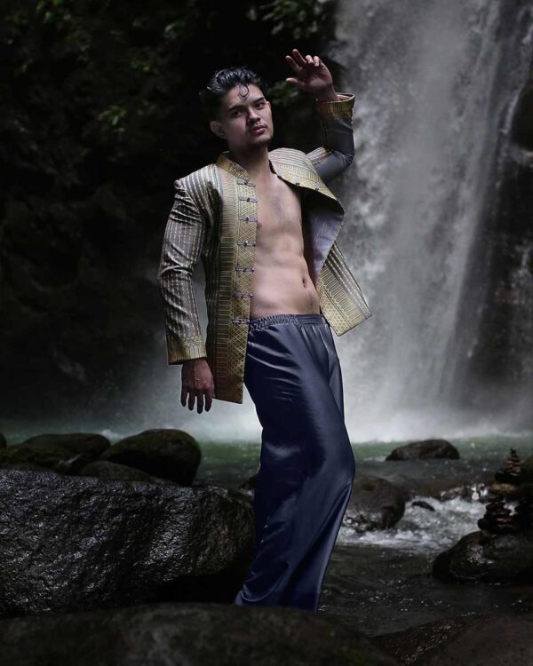 Contemporary Filipino menswear jacket with geometric detailing worn near a waterfall, paired with relaxed trousers