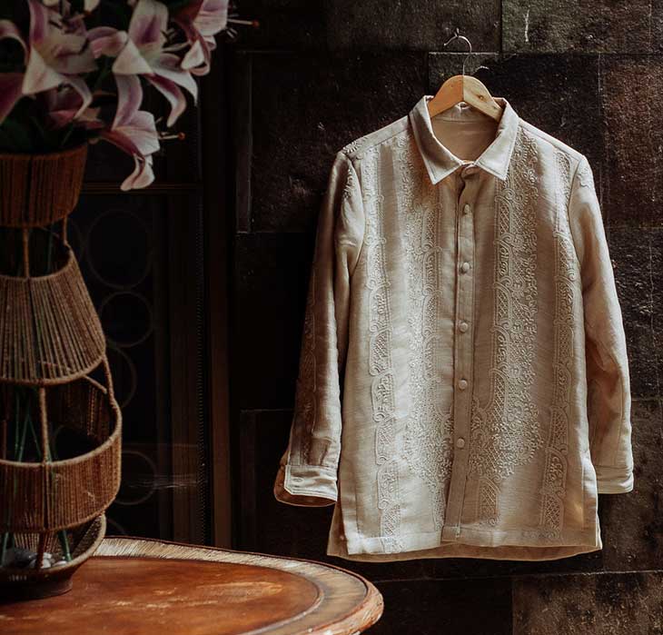 Traditional Barong Tagalog formal shirt with front ornament, hanging on a wooden hanger