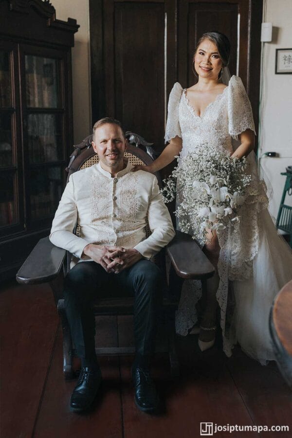 Bride in a detailed lace Filipiniana wedding dress beside a groom wearing a Coat Barong Tagalog with understated ornamentation