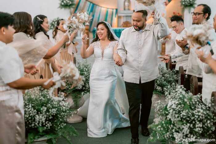Bride in a modern European-style wedding dress beside a groom in a Barong Tagalog with botanical embroidery